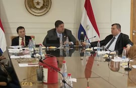 Dionisio Amarilla gesticula mientras Celeste Amarilla escucha atentamente en un ambiente formal con una bandera paraguaya detrás.