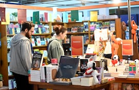 Hombre con barba en sudadera gris observa a mujer con cabello recogido y sudadera verde, rodeados de libros y estanterías.