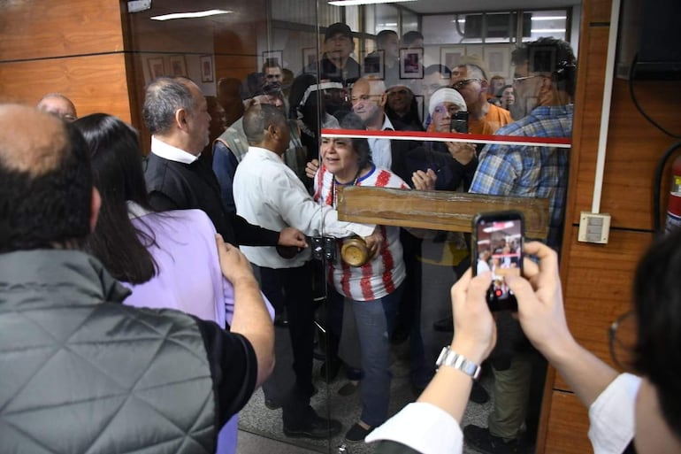 Mujer en camiseta de rayas conversando intensamente, rodeada de personas con interés en un ambiente tenso y comprometido.