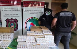 Dos oficiales de policía, uno con capucha, revisan cajas de cigarrillos en ambiente de investigación criminal.