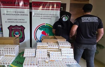 Dos oficiales de policía, uno con capucha, revisan cajas de cigarrillos en ambiente de investigación criminal.