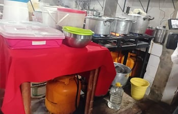 Mesa con mantel rojo, recipiente rosa, bol verde y olla de acero inoxidable en cocina sin personas presentes.