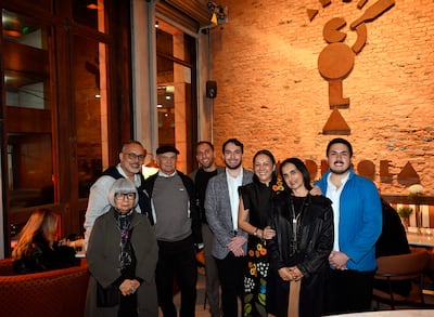 Una mujer en vestido negro se destaca entre ocho personas sonrientes en un interior acogedor con decoración de ladrillo expuesto.