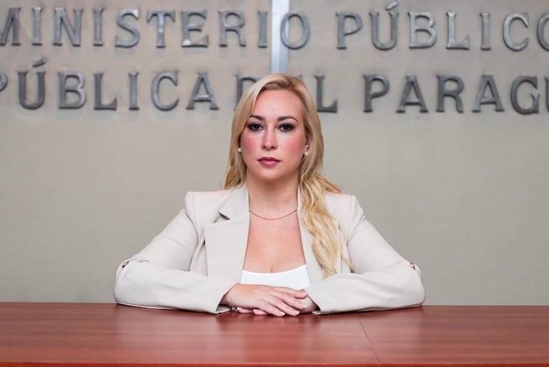 Vivian Coronel Peralta, con blazer claro y blusa blanca, sentada en su oficina con expresión seria y manos cruzadas sobre el escritorio.