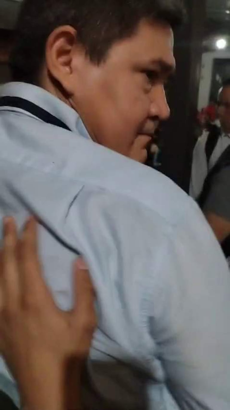 Hombre de camisa clara recibe un gesto de contacto físico en un ambiente cercano y social.