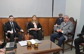 Isaías Fretes en traje negro y Silvia González en atuendo formal claro conversan en reunión con otros hombres en ambiente profesional.