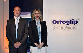Dos personas en ambiente moderno: hombre con traje oscuro y mujer con blazer negro, ambos sonrientes ante el logotipo de Orfoglip.