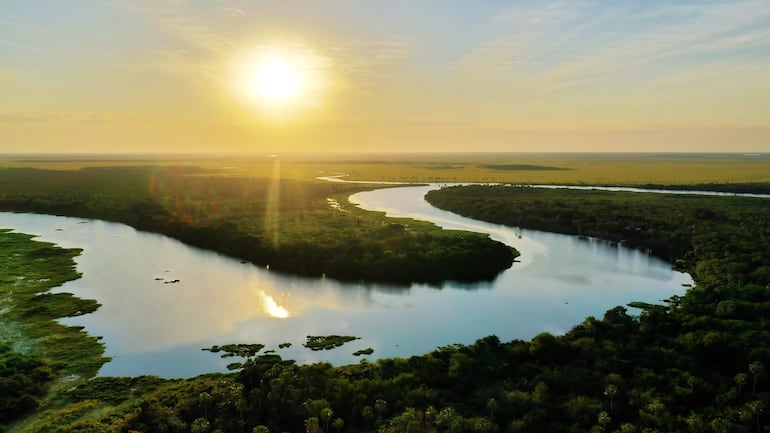 Paisaje del Pantanal Paraguayo con un río serpenteante y vegetación densa, iluminado por el sol en el horizonte.