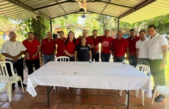 Grupo de hombres en camisetas rojas y una mujer reunidos alrededor de una mesa con mantel blanco en un ambiente tranquilo.