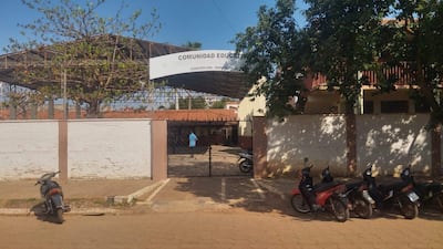 Entrada de la Comunidad Educativa en Concepción, con cartel y motocicletas estacionadas a la izquierda, y un árbol que brinda sombra.