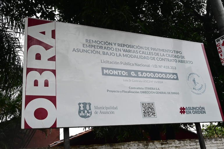 Cartel de obra pública informando sobre el pavimento tipo empedrado en Asunción, rodeado de vegetación.