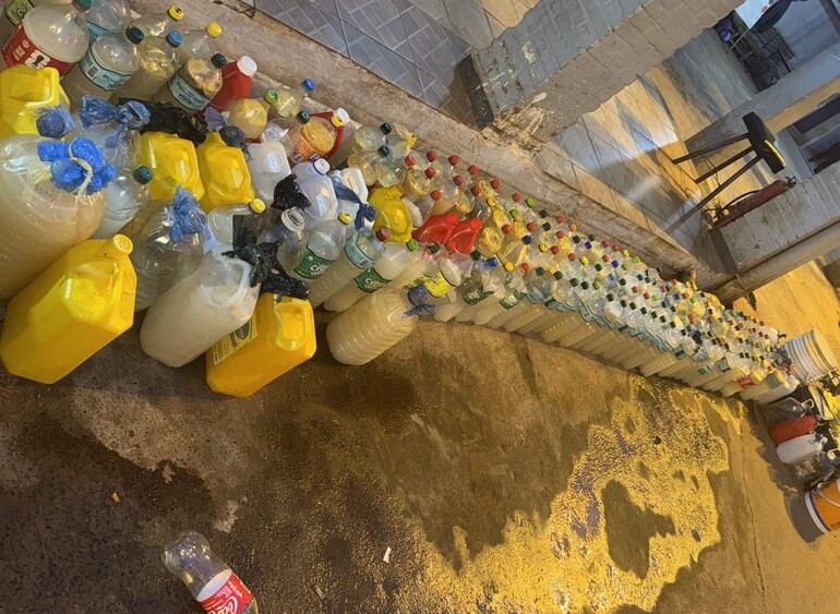Botellas de plástico alineadas en concreto, luces artificiales iluminan el ambiente nocturno. Variedad de colores y tamaños visibles.