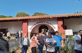 Grupo de personas, algunas con expresiones alegres, saliendo de la Escuela Superior Rca del Ecuador en un día soleado.