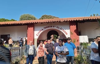 Grupo de personas, algunas con expresiones alegres, saliendo de la Escuela Superior Rca del Ecuador en un día soleado.