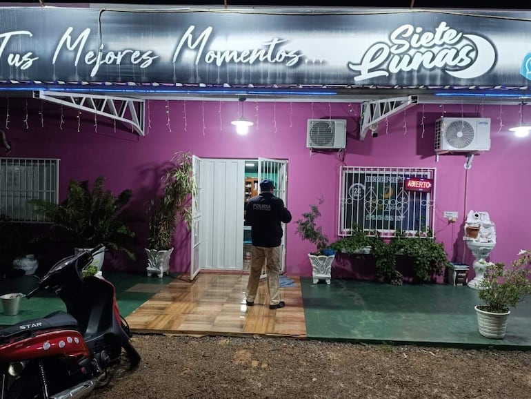 Hombre de espaldas en chaqueta oscura frente a fachada rosa del Motel Siete Lunas, con motocicleta estacionada a la izquierda.