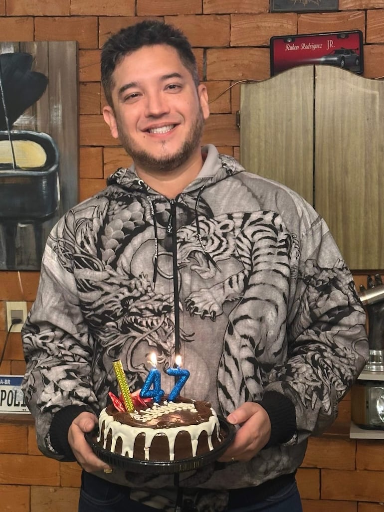 Junior Rodríguez sonríe con una torta de cumpleaños con velas, vestido con camiseta de tigres en un entorno festivo.
