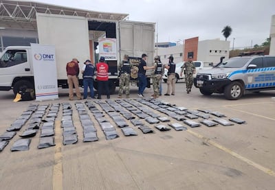 Agentes en uniformes con chalecos identificativos revisan un camión cargado de paquetes negros en un ambiente urbano.