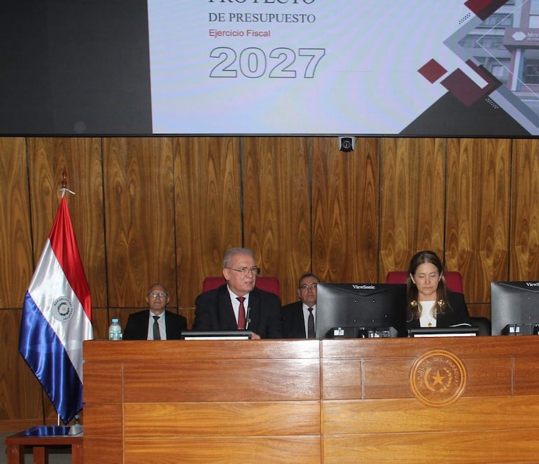 Emiliano Rolón Fernández en traje oscuro habla ante la comisión, mientras una mujer castaña escucha atentamente en un ambiente formal.