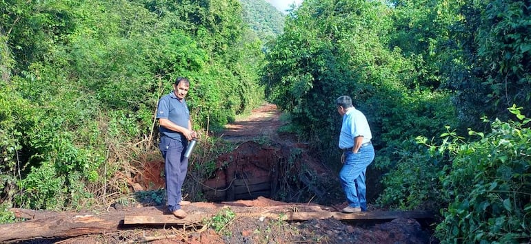 Aldo Lezcano, vestido informalmente, observa un agujero en el terreno mientras sostiene un objeto cilíndrico, rodeado de vegetación densa.