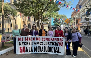 Siete mujeres de pie sosteniendo pancarta de protesta en calle, con expresión firme y decidida.