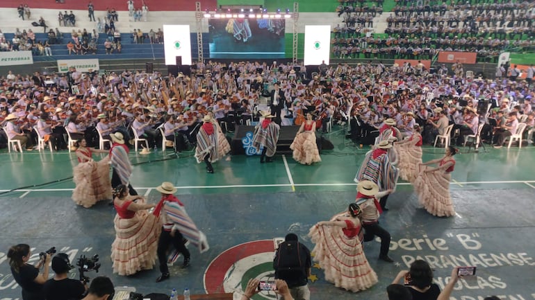 Bailarines con trajes tradicionales y músicos en camisetas moradas, disfrutando de un ambiente festivo.