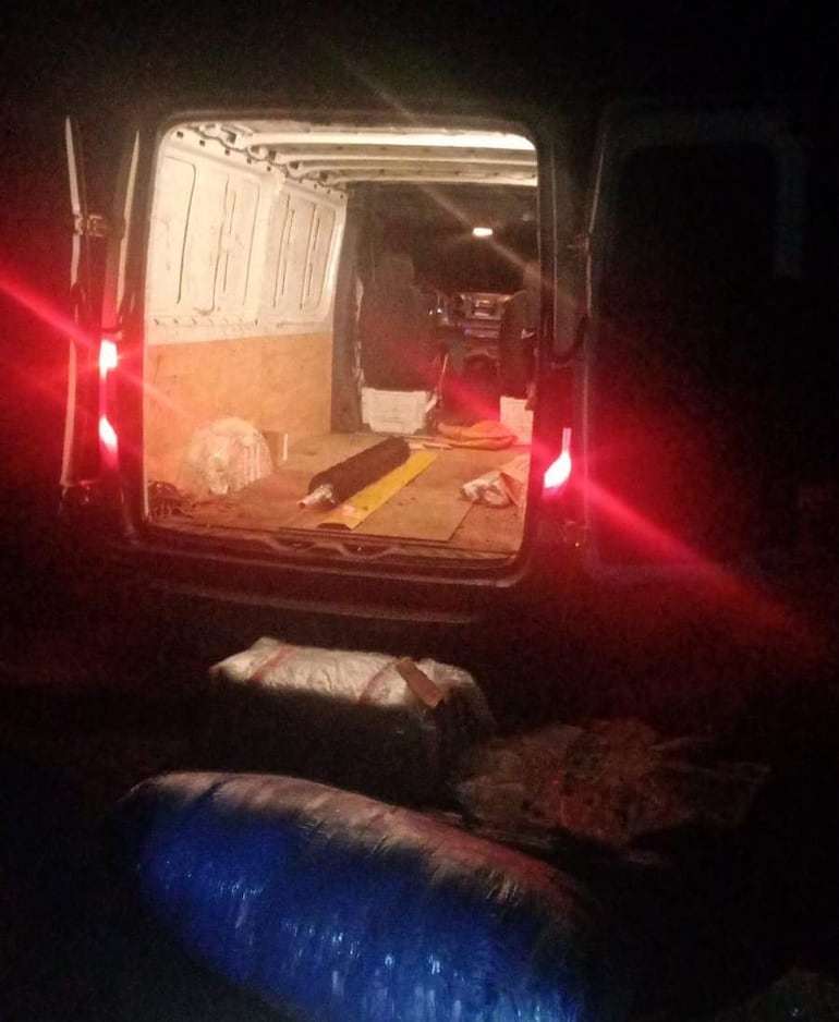 Furgoneta abierta, interior iluminado con bultos plásticos y un bulto azul en el suelo de madera.