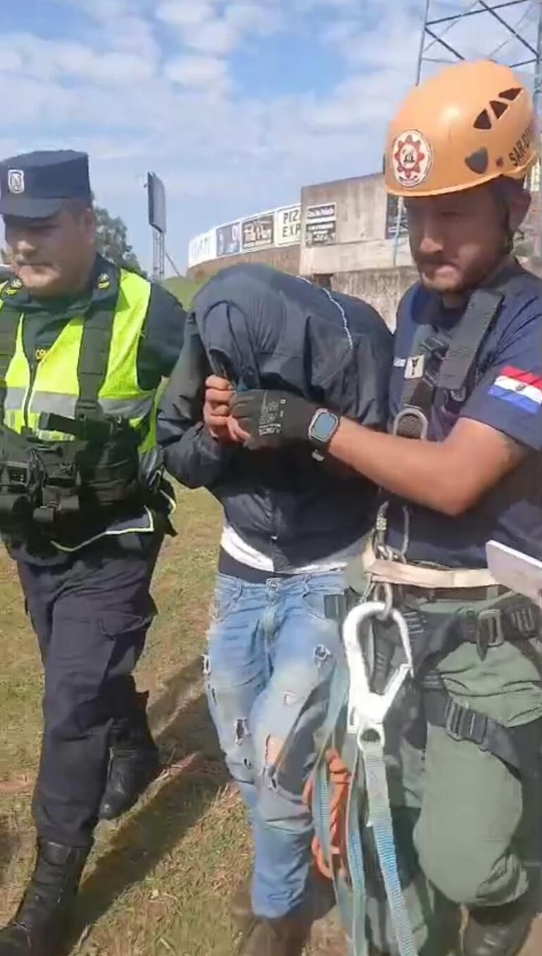 Un agente policial y un bombero junto al hombre que trepó una torre de 45 metros y amenazó con lanzarse.