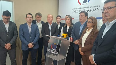 César Sosa en el podio con traje oscuro, mientras once personas, en su mayoría con trajes oscuros, escuchan atentamente en una sala de conferencias.
