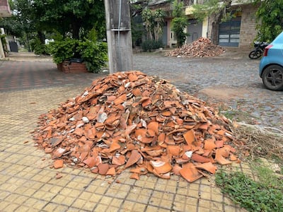 Montículo de escombros de cerámica y tejas en una vereda urbana, con un vehículo azul estacionado al fondo.