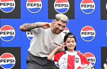 Joven rubio con tatuajes y niño con camiseta de selección paraguaya posan felices, sosteniendo un balón de fútbol decorado.
