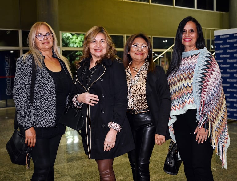 Cuatro mujeres sonrientes en el Teatro Lírico, una con abrigo negro y otra con chaqueta colorida, posando juntas en ambiente iluminado.