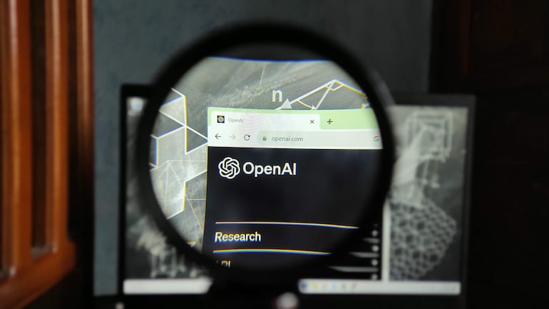 Pantalla de computadora con página de OpenAI y elementos gráficos abstractos de fondo.