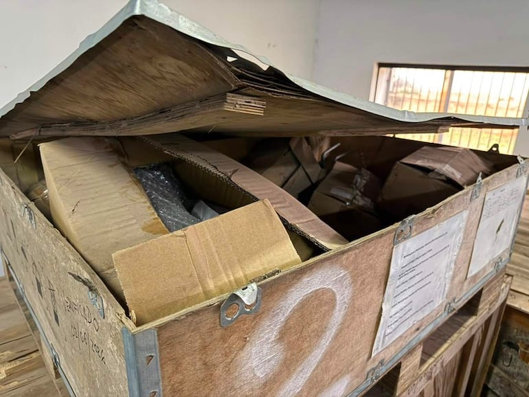 Contenedor de madera parcialmente abierto con cajas desordenadas en un ambiente de almacenamiento.