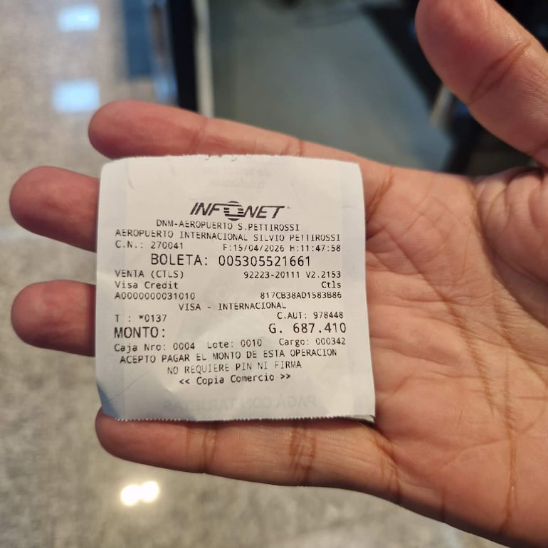 Recibo en mano con información de transacción en el aeropuerto, destacando el monto y método de pago con tarjeta Visa.