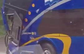 Autobús azul y amarillo volcado en la carretera, sin personas visibles en el entorno.