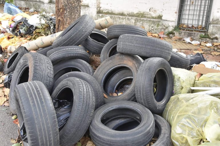Montón de neumáticos apilados entre basura en una zona urbana sin personas presentes.