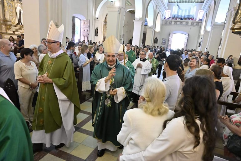 Adalberto Martínez Flores y Alda Cardozo en ceremonia religiosa, rodeados de sacerdotes con vestimenta litúrgica en un ambiente de iglesia.