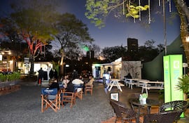 Grupo de mujeres conversando en un ambiente exterior con mesas y sillas, rodeado de árboles con luces.