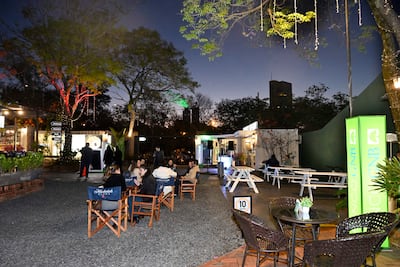 Grupo de mujeres conversando en un ambiente exterior con mesas y sillas, rodeado de árboles con luces.