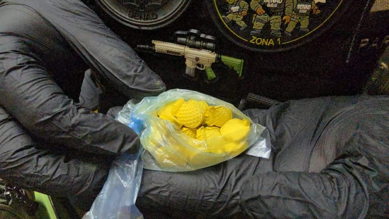 Primer plano de una mano con guante negro sosteniendo una bolsa plástica con materiales amarillos, en un ambiente relacionado con seguridad.