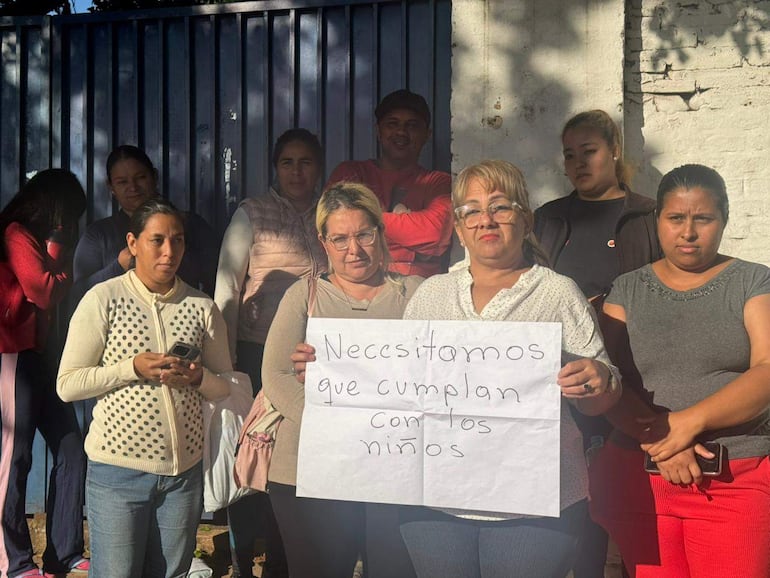 Una mujer sostiene un cartel que dice 'Necesitamos que cumplan con los niños', rodeada de otras personas en una protesta.