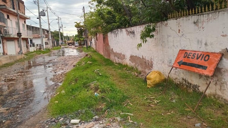 Cartel de desvío en calle de barrio San Pablo rodeada de barro y agua estancada, con costal amarillo cercano.