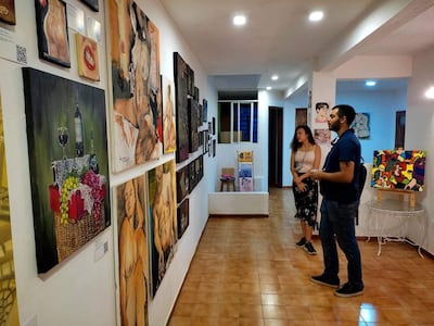 Mujer de cabello rizado escucha al hombre de mochila en galería con pinturas de cuerpos humanos y frutas.