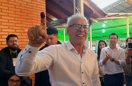 Rigoberto Chamorro sonriente, con cabello blanco y gafas, levanta el dedo marcado con tinta en un centro de votación.