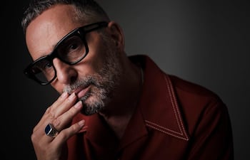 Drexler, con camisa roja y gafas grandes, muestra una expresión reflexiva mientras se sostiene la cara con una mano.
