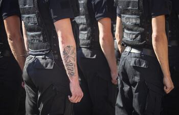 Grupo de oficiales de policía en uniforme oscuro y chalecos tácticos, con un tatuaje visible en el brazo de uno de ellos.
