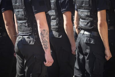 Grupo de oficiales de policía en uniforme oscuro y chalecos tácticos, con un tatuaje visible en el brazo de uno de ellos.