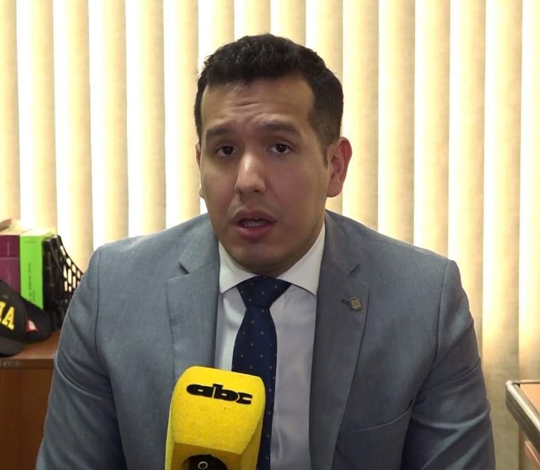 Christian Manuel Benítez Cáceres en traje gris, hablando a la cámara con micrófono de ABC Color, en un ambiente institucional con objetos sobre la mesa.