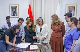 Mujeres y hombres en reunión formal, con documentos sobre la mesa y expresiones de seriedad y compromiso. Banderas de Paraguay visibles en el fondo.