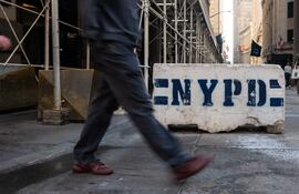 Personas pasan junto a los controles de seguridad de la policía de Nueva York (NYPD) en Wall Street, mientras la ciudad se encuentra bajo un "Entorno de Amenaza Elevada".